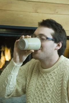 Young man drinking hot beverage by fireplace 写真素材