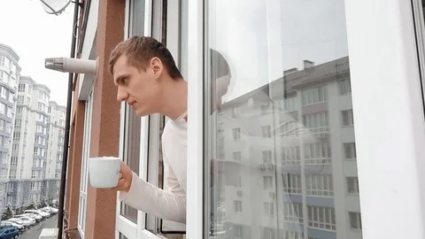 Young man is drinking hot coffee or tea, looking out the window 스톡 동영상 126921020