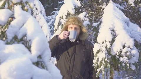 A young man drinking a hot tea in a winter forest. Beautiful sunny morning in Video stock 83733451