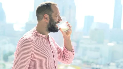 Young man drinking milk and admire view from window at home, super slow motion  스톡 동영상 72225012