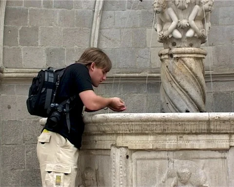 Young man drinking from Onuphrius Little Fountain on Luza Square in Dubrovnik Stock Footage 106607223