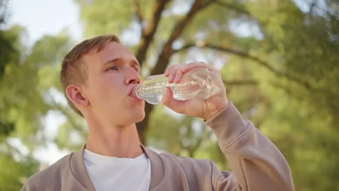 Young man drinking pure water from a plastic bottle outdoors in a sunny par.. Vídeo Stock 339534399