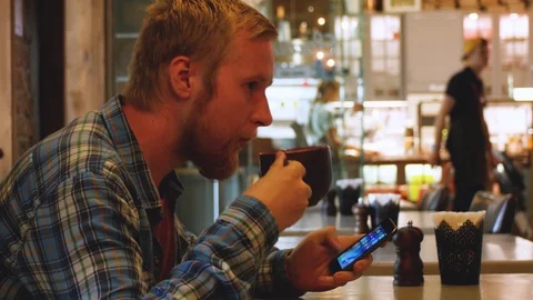 Young man drinking tea in a cafe with a phone in his hands. student lunch at a Stock-Footage 107383946
