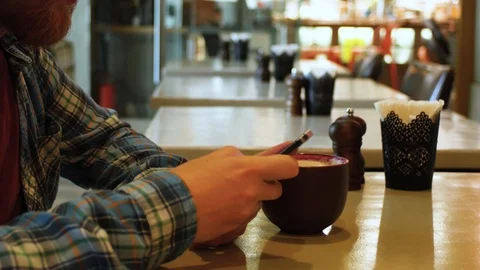 Young man drinking tea in a cafe with a phone in his hands. student lunch at a Stock Footage 107384525