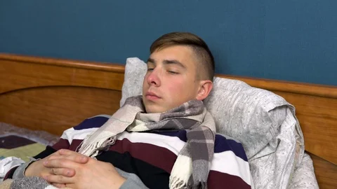 A young man is drinking tea with lemon. The guy is sick lying on the bed with a Stock Footage 115847533