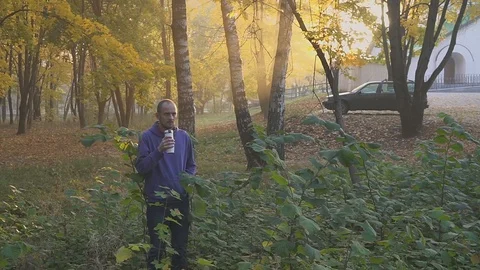 Young man drinking tea or coffee from a thermocup in autumn park Video stock 96276459