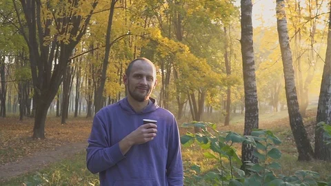 Young man drinking tea or coffee from a paper cup in autumn park Video stock 96277022