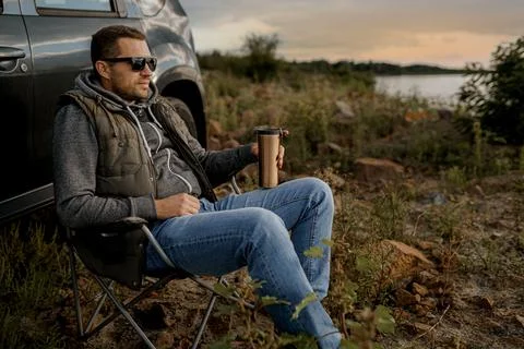Young man is drinking tea while fishing. Outdoor picnic concept Stock Photos