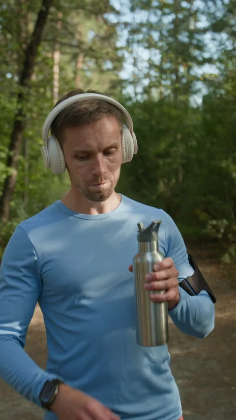 Young Man Drinking Water and Checking Time, Taking Break from Jogging in Forest Stock Footage 315183889