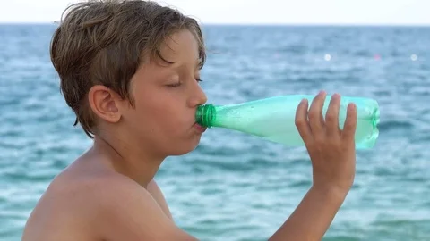 Young man drinking from a Water Bottle on the beach Vidéo 79852926