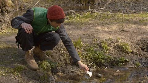 Young man drinking water from a forest river Stock Footage 129081213