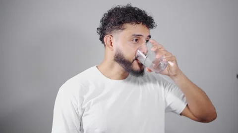 Young man drinking water on gray background Stock Footage 315051556