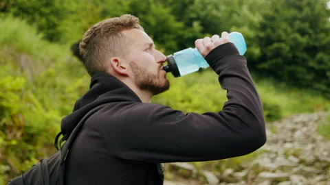 Young man drinking water at a hike in the mountains 4K. Video stock 234617475