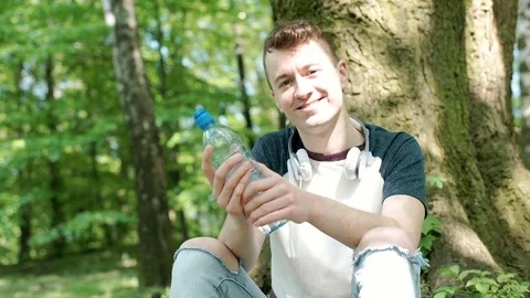 Young man drinking water in the park and smiling to the camera, steadycam shot 스톡 동영상 76385264