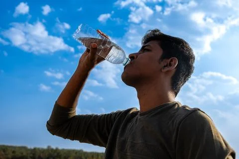 Young man drinking water from a plastic bottle on the background of the blu.. Stock Photos
