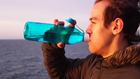 A young man drinking water from a reusable glass bottle Video stock 131490472