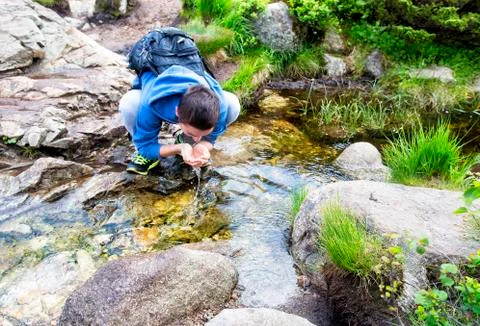Young man drinking water from a spring. Stock Photos