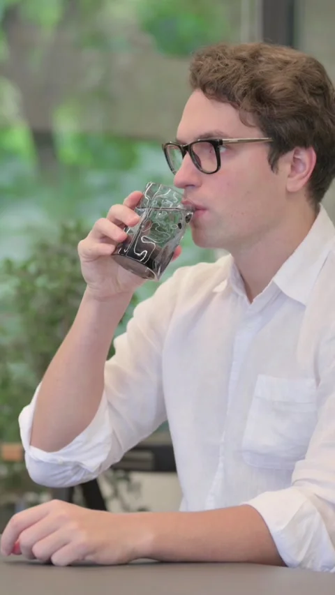 Young Man Drinking Water While Sitting in Office, Vertical Video 库存影片 340032822