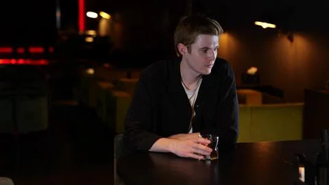 Young man drinking whiskey while sitting in a restaurant in the evening and Stock Photos