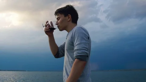 Young man drinking wine in sunset by the sea Stock Footage 81391457