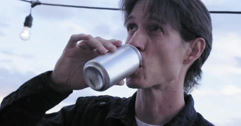 Young man drinks beer from a can in at dusk 4K Stock Footage 63498317