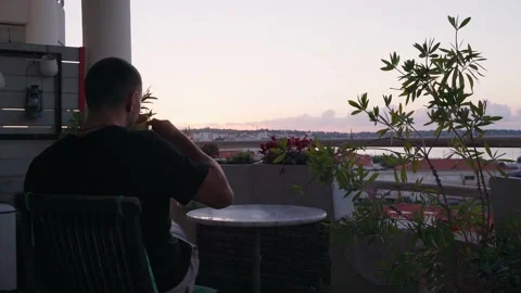 Young Man drinks coffee from cup on balcony and watching sunrise in the morning Stock Footage 191641005
