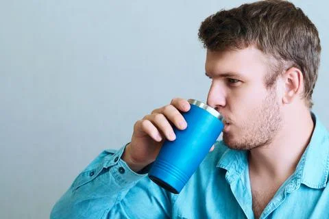 Young man drinks drink or medicine from thermo mug. Portrait of man from side on Stockfoto's