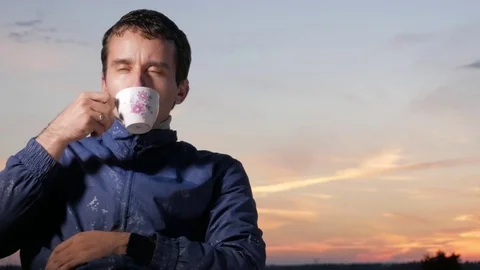 A young man drinks a hot drink from a mug at sunset. Beautiful sky behind. Stock Footage 76923007