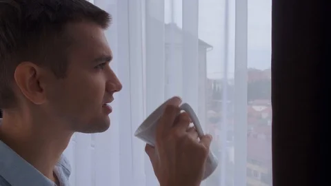 A young man drinks a hot drink near the window in the morning. Close up Stock Footage 120606591