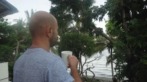 A young man drinks a hot drink on a background of beautiful tall palm trees. Stock Footage 133460735