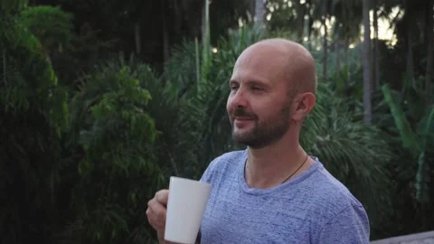 A young man drinks a hot drink on a background of beautiful tall palm trees. 動画素材 133509688