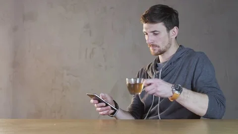 Young Man Drinks Tea and Uses his Mobile Stock Footage 69172486