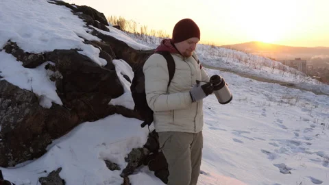 A young man drinks tea or coffee from a thermos on a hill near the city. Stock Footage 85684259