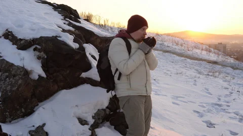 A young man drinks tea or coffee from a thermos on a hill near the city. 스톡 동영상 92096764