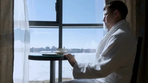 A young man drinks tea sitting by the window and writes an SMS message Stock Footage 78173462