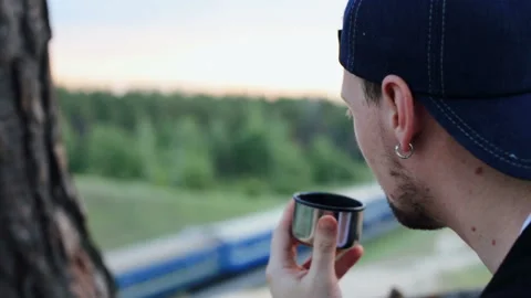 A young man drinks tea from a thermos in the forest area Stock Footage 90385829