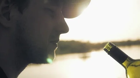 Young man drinks from a throat red wine on a sunset and lake background. Close Stock Footage 76214946