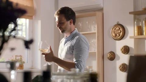 Young man drinks white wine from the big glass on the kitchen in the sunny Stock Footage 97937016