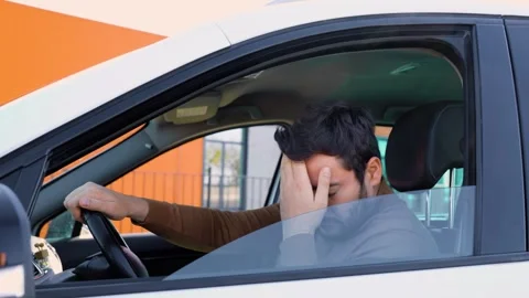 A young man driver stopped while sitting behind the wheel and holds his head Stock Footage 300255621