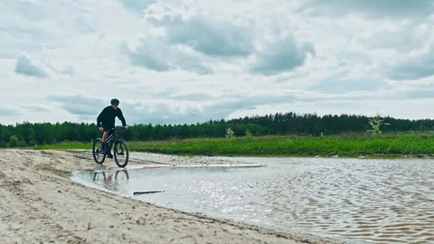 Young man drives into a large puddle on a black mountain bike. Cyclist rides  Stock Footage 130769514