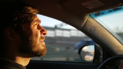 Young man driving a car. the setting sun shines in the eyes of the driver. Stock Footage 144555030