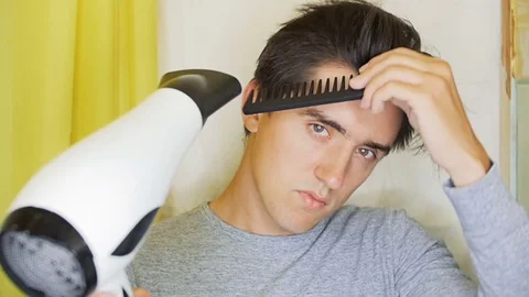 A young man is drying his hair with a hair dryer. Stock Footage