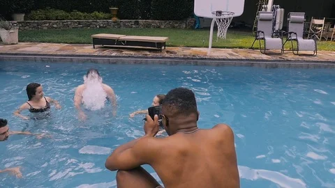 Young man dunks his head in a pool while another man films it with his phone 스톡 동영상 121976125