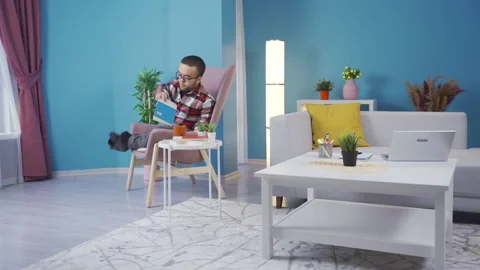 Young man with dwarfism is reading his book on the sofa at home. Stock Footage 230976785