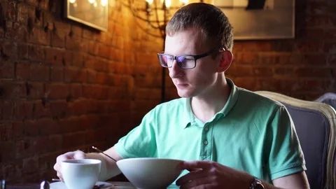 Young man eating and drinking tea or cofe, breakfast in restaurant Stock Footage 73127167