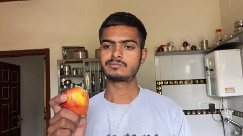 Young Man Eating an Apple in the Kitchen and Giving a Thumbs Up to the Camera Stock Footage 321388472