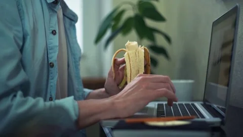 Young man eating banana using laptop at home. Man working out off office. Stock Footage 82932217