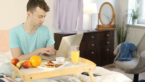 Young man eating breakfast in bed and using notebook, steadycam shot Stock-Footage 76527720