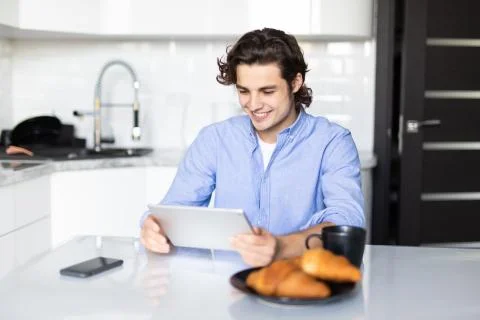 Young man eating breakfast while using digital tablet in modern kitchen Stock Photos
