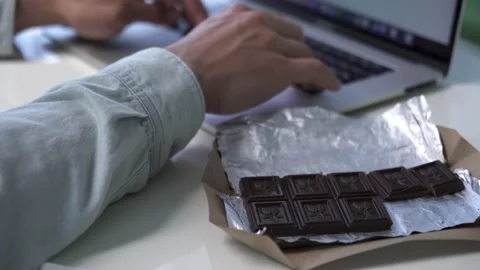 Young man eating chocolate while working with laptop in office. Close up Stock Footage 136666852